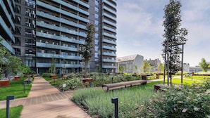 Un bâtiment moderne à structure à plusieurs étages, doté d’un jardin aménagé avec des bancs et d’un sentier.