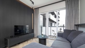 Un salon moderne doté d’un grand téléviseur à écran plat, d’un canapé gris et d’une petite table agrémentée d’objets décoratifs.