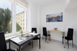 A modern dining area with a table, chairs, a view of buildings, and a cityscape painting on the wall. - Spacious Apartment with Air Conditioning | Downtown (Warszawa)