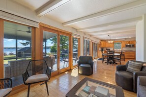 Amplia sala de estar con vista a un lago, piso de madera y muebles modernos.