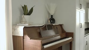 A piano in a corner of a room with a white wall, a plant, and a vase.
