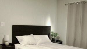 A neatly made bed with a dark headboard, a bedside table with a lamp, and a potted plant.