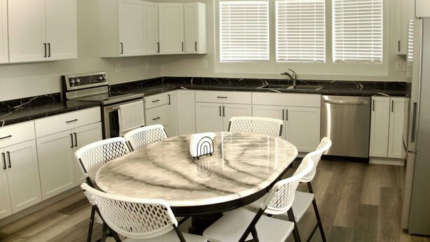 A modern kitchen with white cabinets, a black countertop, a round dining table with chairs, and a built-in oven.