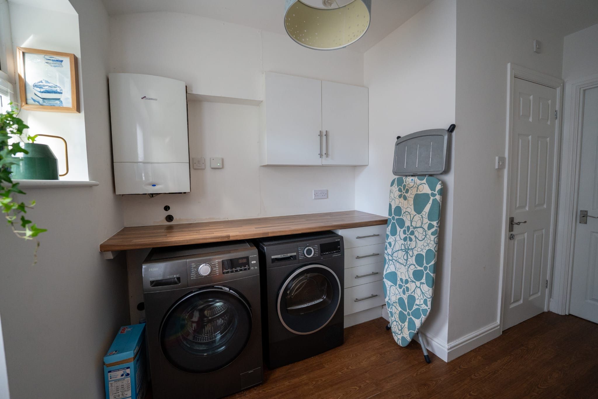 A compact kitchen with a washing machine, a drying rack, and a small cabinet.