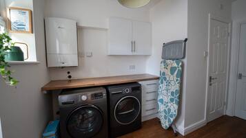 A compact kitchen with a washing machine, a drying rack, and a small cabinet.