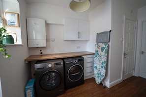 A compact kitchen with a washing machine, a drying rack, and a small cabinet.