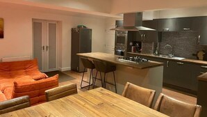 Een compacte keuken met moderne apparatuur, een eethoek met een houten tafel en stoelen, en een klein schiereiland met barkrukken.