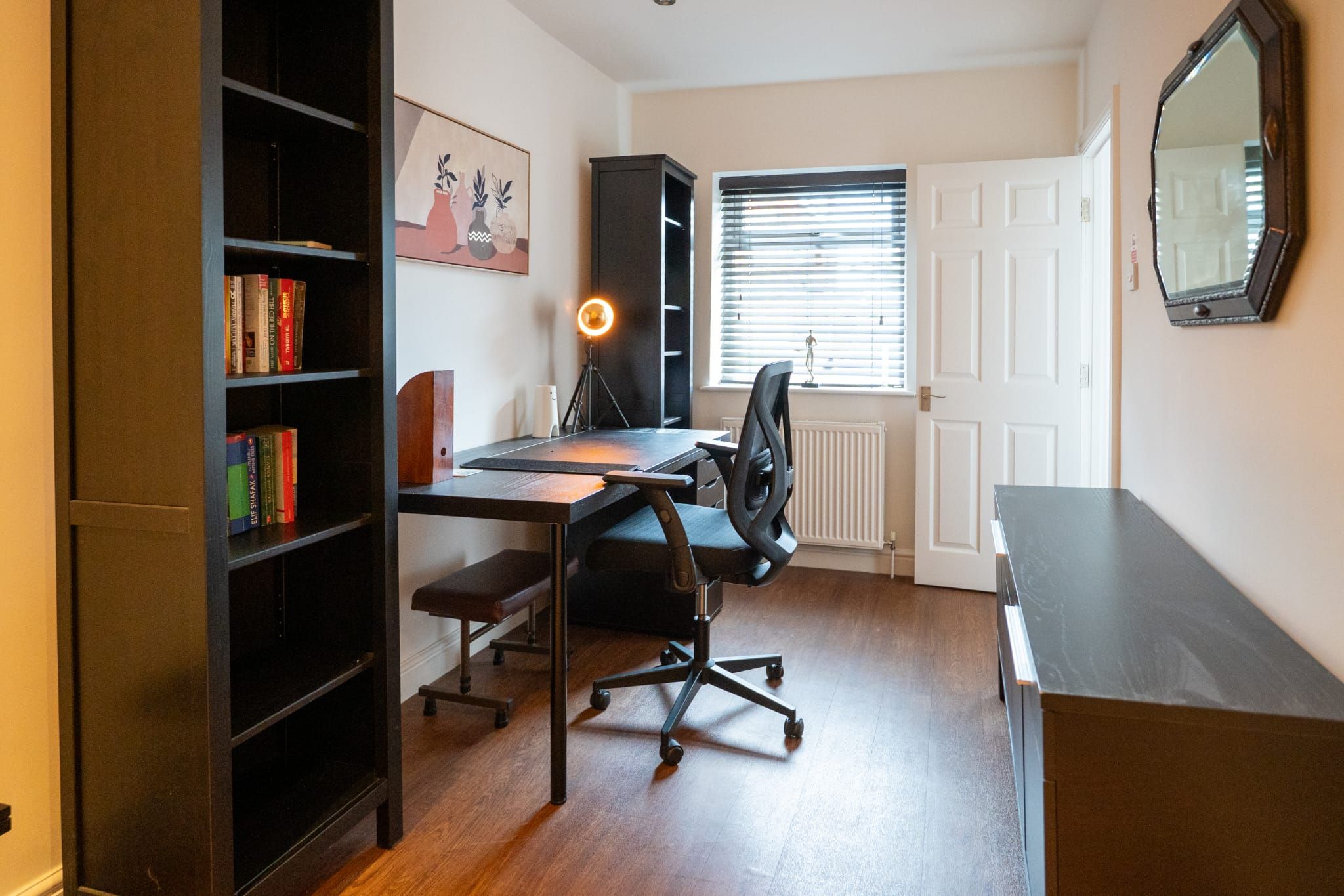 A study room with a desk, chair, bookshelf, and a window with blinds.