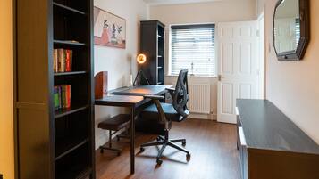 A study room with a desk, chair, bookshelf, and a window with blinds.