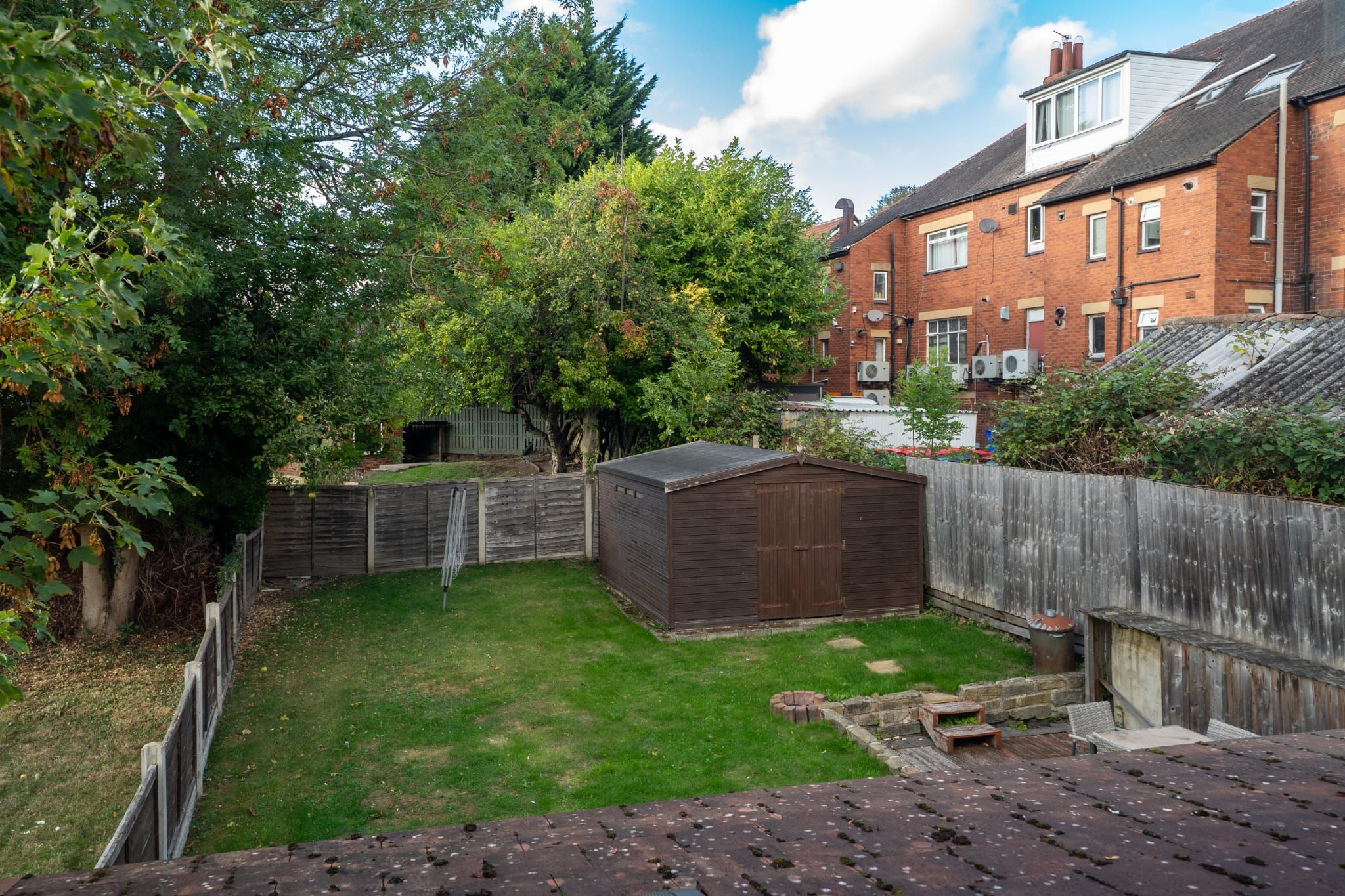 A backyard with a wooden shed, a fenced area, and a brick house in the background.