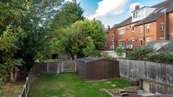 A backyard with a wooden shed, a fenced area, and a brick house in the background.