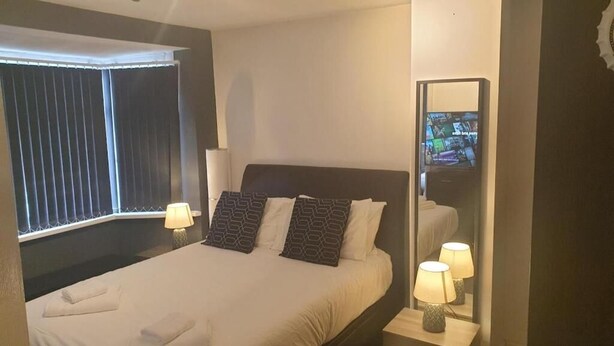 Een hotelkamer met een bed, bedlampen, een raam met zonwering, een spiegel en een televisietoestel.