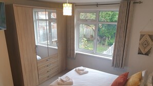 Een slaapkamer met een bed, een kledingkast, een raam met gordijnen en uitzicht op groen.
