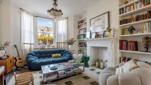 A living room with a blue sofa, a bookshelf, a fireplace, and a chandelier. - Family House London - 4 bedrooms, sleeps 8/9, garden, near Notting Hill (London)