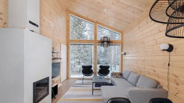 A modern interior with a wooden ceiling, large windows, a gray sofa, black chairs, and a dining table. - Porevillas Iso-Syöte A (Syöte)