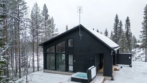 A modern cabin with a large glass window, a wooden deck, and a hot tub. - Porevillas Iso-Syöte A (Syöte)