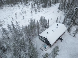 A modern cabin with a large deck, surrounded by a snowy forest.