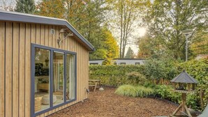 A modern wooden building with large windows, a garden with a wooden deck, and a bird feeder. - Knusse Tiny house op de Veluwe (Epe)
