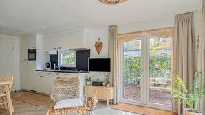 A modern kitchen with white cabinets, a flat-screen TV, and a dining area with wicker furniture. - Knusse Tiny house op de Veluwe (Epe)