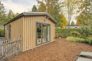 A wooden cabin with a window, surrounded by a garden with mulch and plants.
