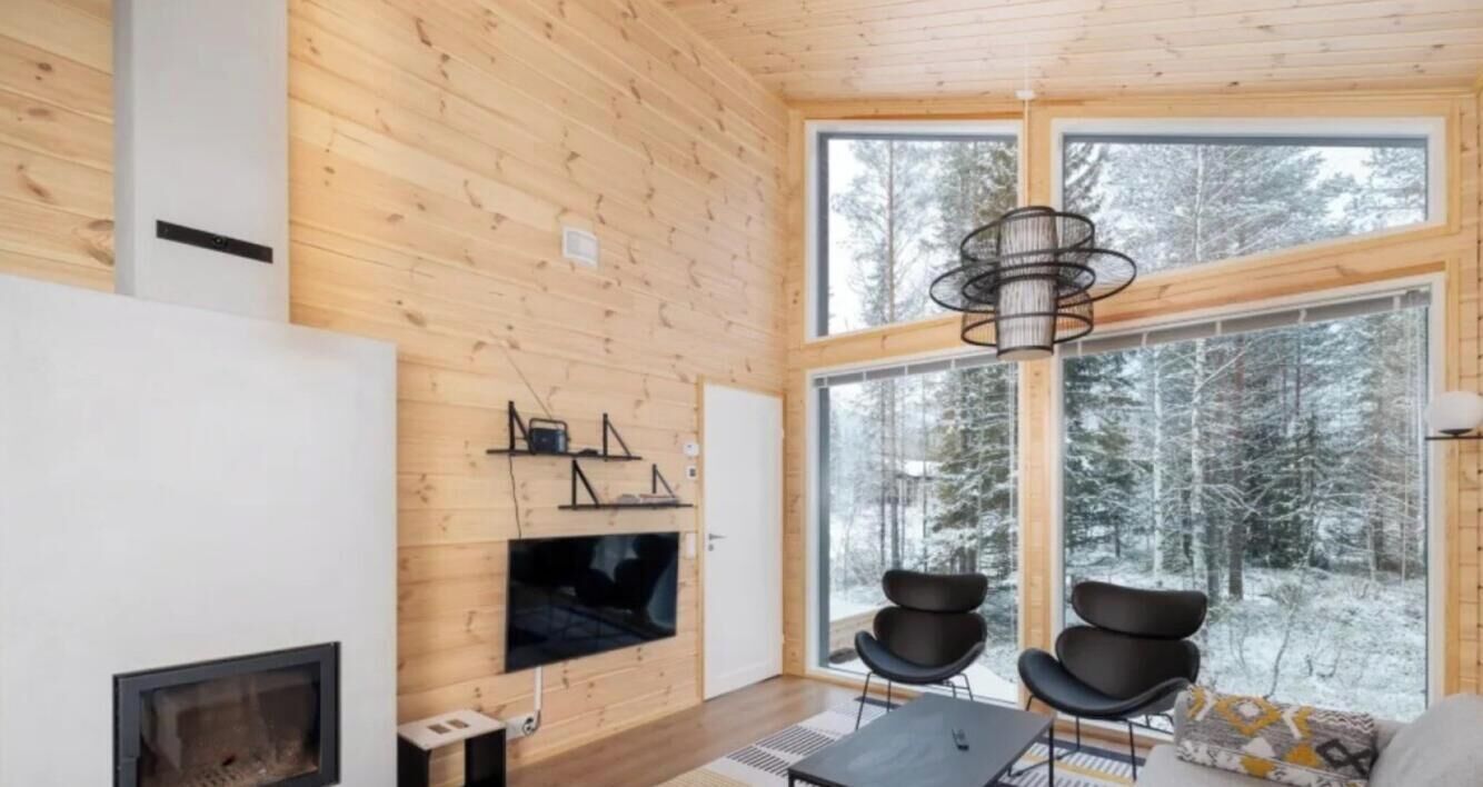 Ein modernes Interieur mit Holzwänden, einem Kamin, einem großen Fenster mit Schneeplatz und einem schwarzen Sessel.