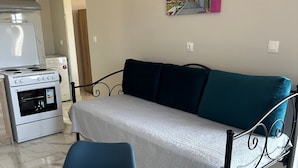 A compact living space with a kitchenette, a sofa, a dining table, and a painting on the wall.