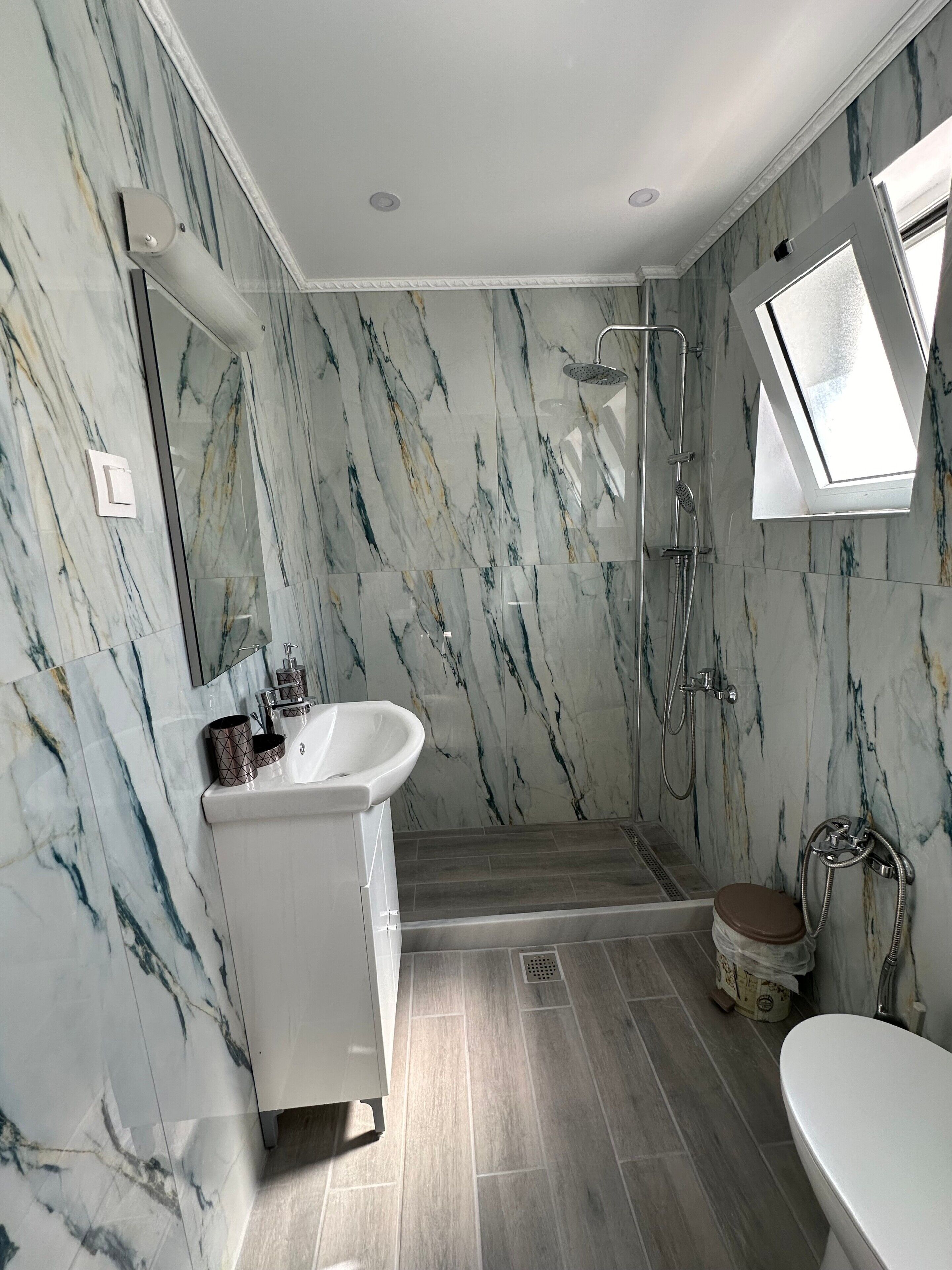 Un baño con pared de mármol, ducha, lavamanos e inodoro.
