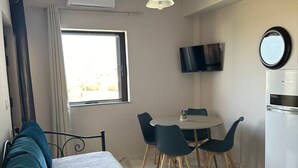 A bedroom with a bed, a window, a dining area with chairs, a TV, and a refrigerator.