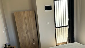 A bedroom with a bed, a wardrobe, a window with blinds, and an air conditioning unit.
