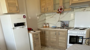 A compact kitchen with a refrigerator, stove, and wooden cabinets.