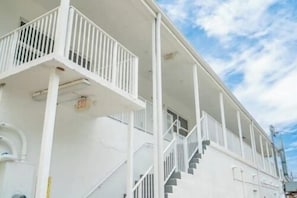Ein weißes Gebäude mit Balkon, Treppen und blauem Himmel.