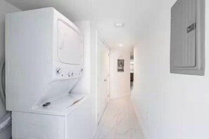 A laundry room with a washer and dryer, a hallway leading to a door, and a light switch on the wall. - The Purple Pelican~Beachfront w/Ocean Balcony~#4 (Fort Lauderdale)