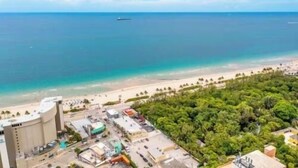 Eine Küstenlandschaft mit Strand, einem Schiffen im entfernten Hintergrund und einem Gebäudekomplex mit Parkplätzen.
