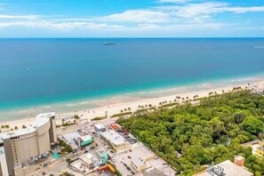A coastal area with a beach, a ship in the distance, and a building complex with parking. - The Purple Pelican~Beachfront w/Ocean Balcony~#4 (Fort Lauderdale)