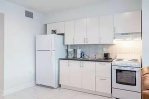 A compact kitchen with white cabinets, a refrigerator, a stove, and a microwave. - The Purple Pelican~Beachfront w/Ocean Balcony~#4 (Fort Lauderdale)
