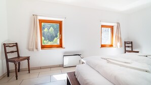 Ein Schlafzimmer mit zwei Fenstern, einem Bett, einem Sessel und einer Heizung.
