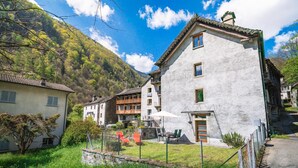 Ein traditionelles Gebäude mit Balkon, Steinmauer und einer Rasenfläche mit Stuhl und Tisch.