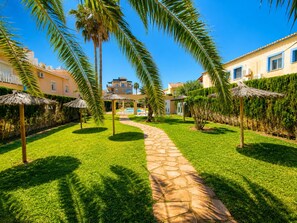 A stone pathway leading to a pool area surrounded by palm trees and a building with multiple windows. - Ap2214 in Denia With 2 Bedrooms and 2 Bathrooms (Denia)