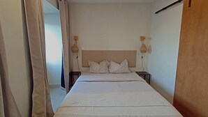 Une chambre à coucher comprenant un lit, deux tables de chevet, une tête de lit et une fenêtre avec des rideaux.