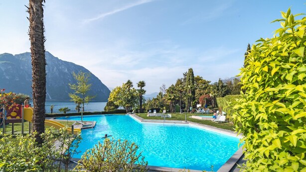 A swimming pool with a mountain backdrop, surrounded by lush greenery and a clear sky. - Bissone   Campione Lake Pool & Relax (Bissone)