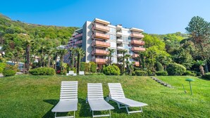 A modern multi-story hotel with balconies, a grassy lawn, and lounge chairs. - Bissone   Campione Lake Pool & Relax (Bissone)