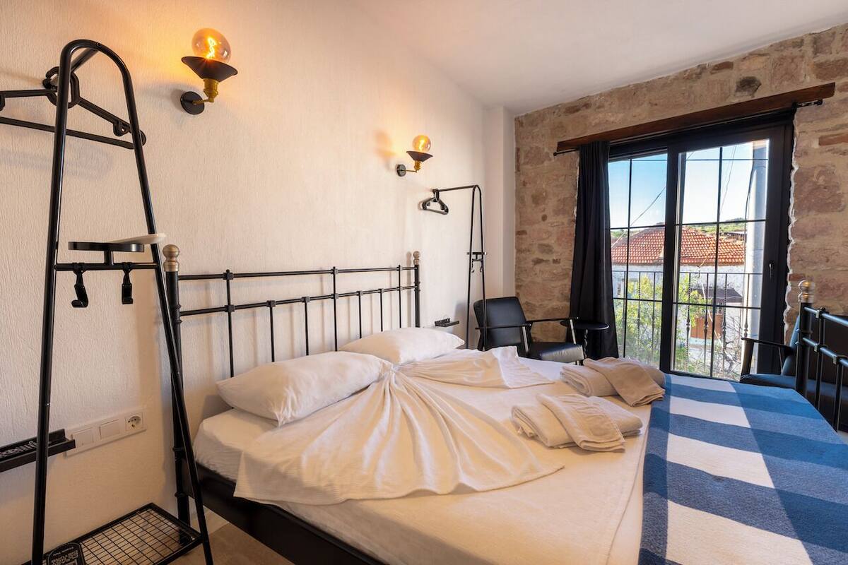 Una habitación de hotel con una cama, dos lámparas de pared, una silla y un balcón con vistas.