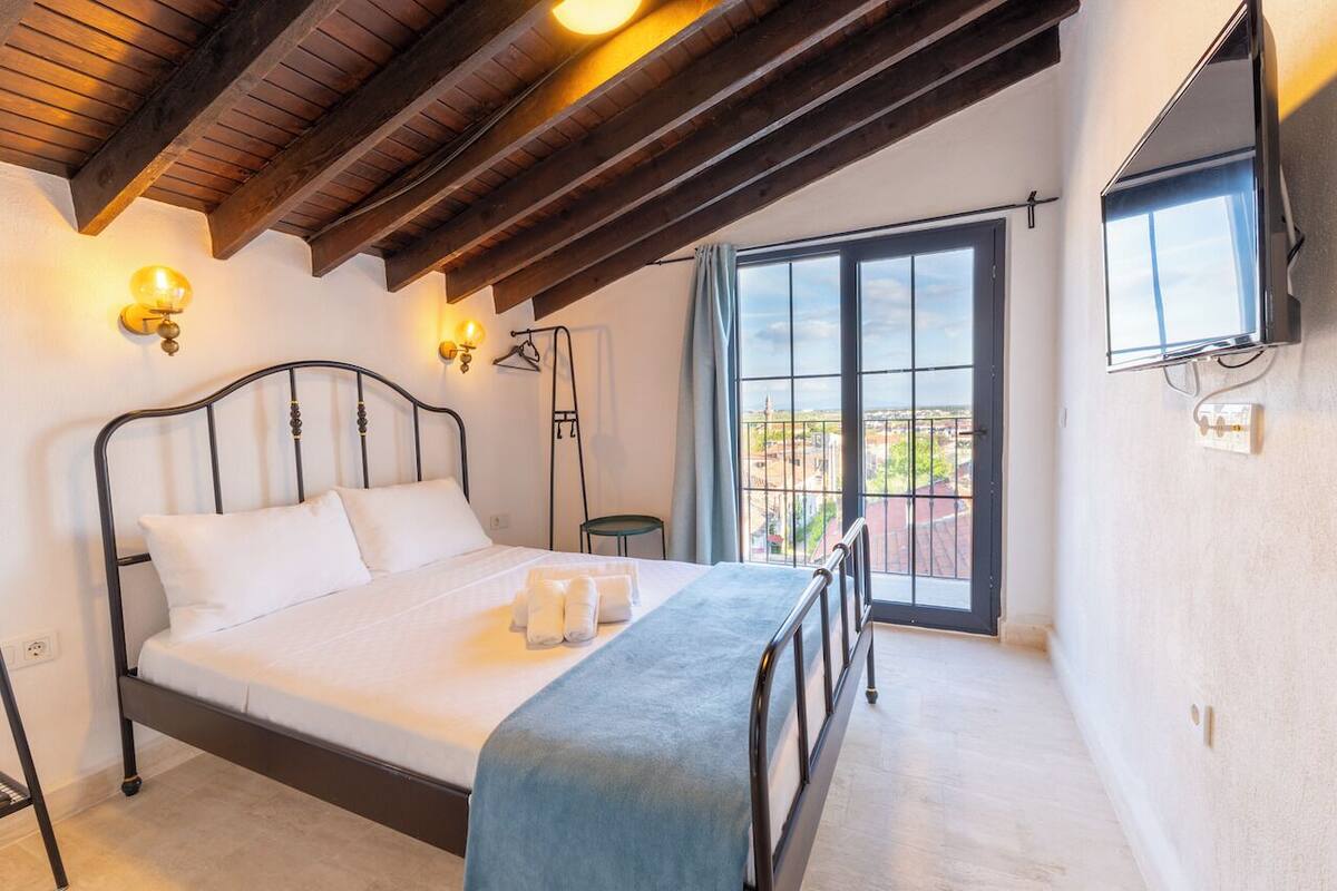 Un dormitorio con cama, ventana, televisor y balcón.