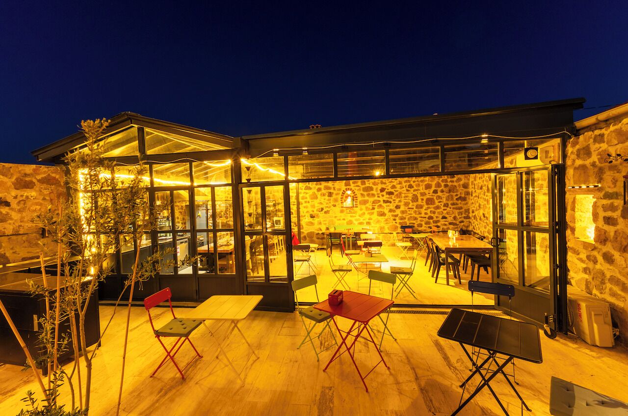 An outdoor dining area with tables and chairs, a stone wall, and a glass enclosure.