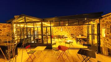 An outdoor dining area with tables and chairs, a stone wall, and a glass enclosure.