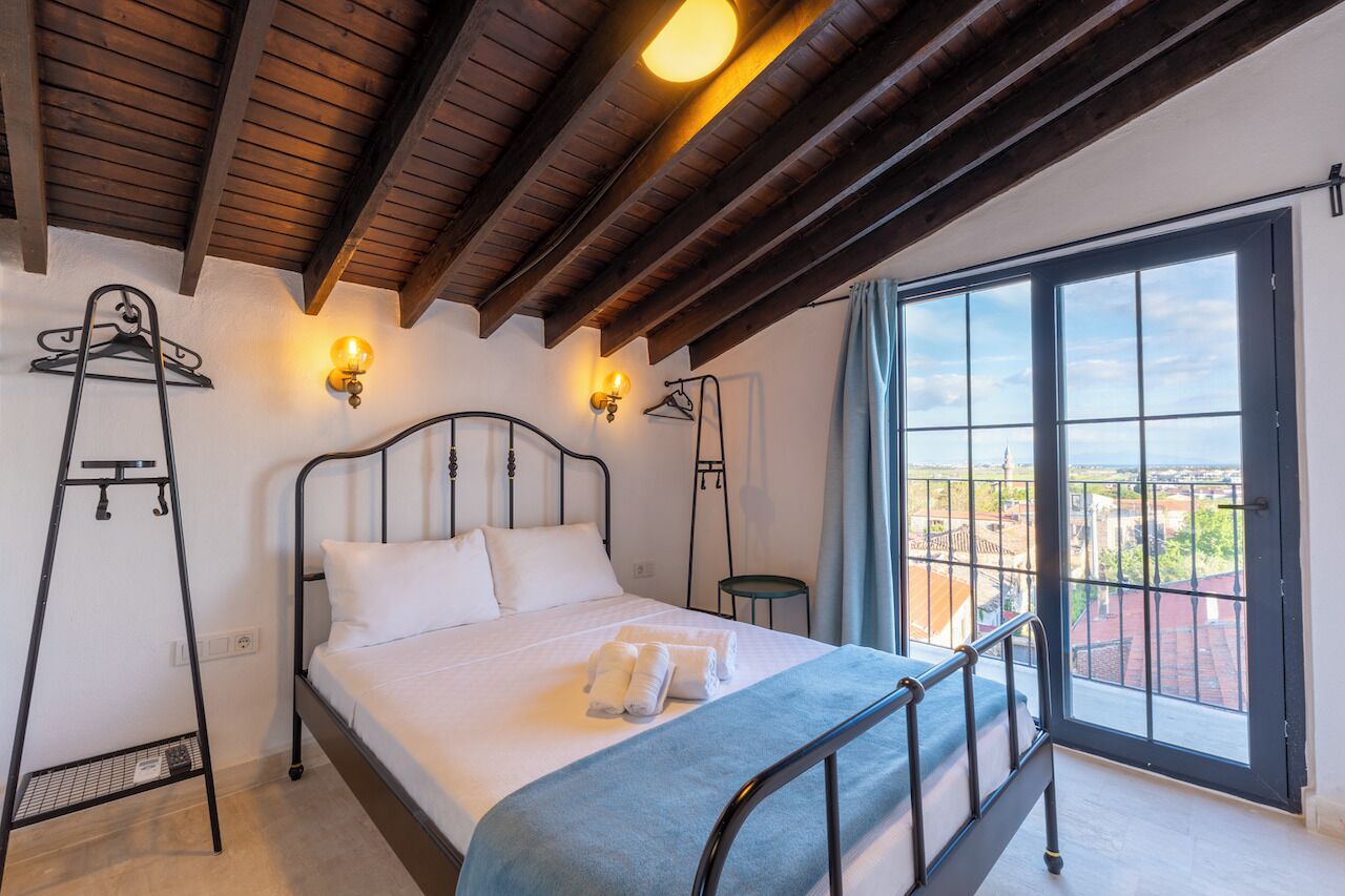 A bedroom with a bed, bedside lamps, a window with a view, and a balcony.