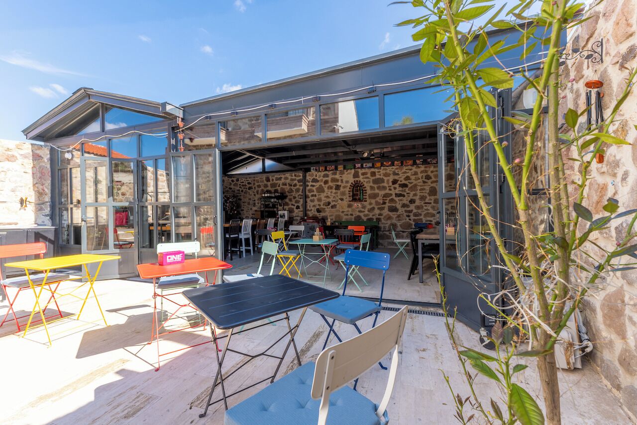 An outdoor seating area with tables and chairs, a stone wall, and a glass enclosure.