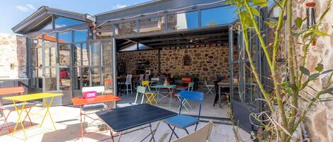 An outdoor seating area with tables and chairs, a stone wall, and a glass enclosure.