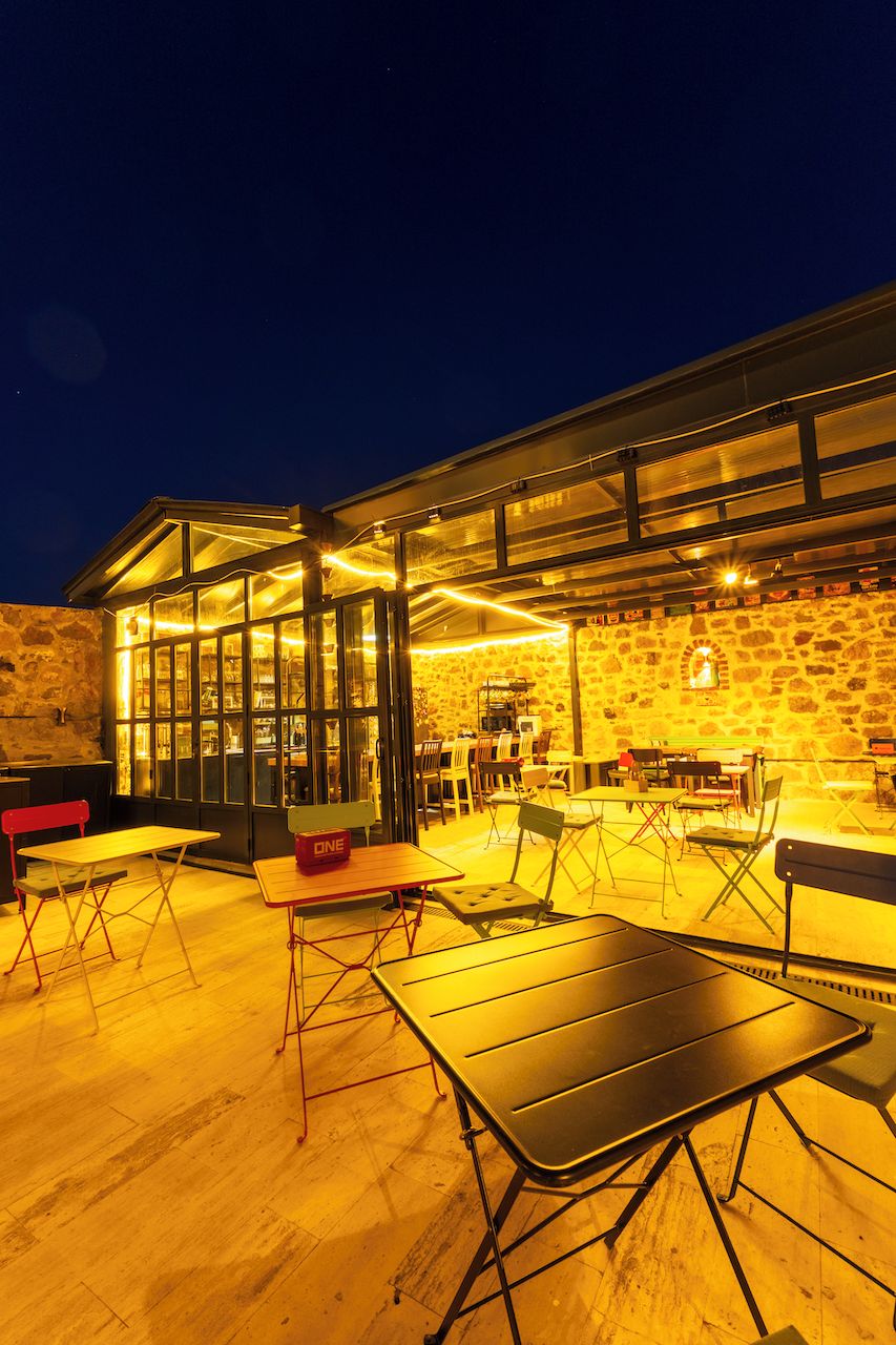 An outdoor seating area with tables and chairs, a stone wall, and a glass enclosure.