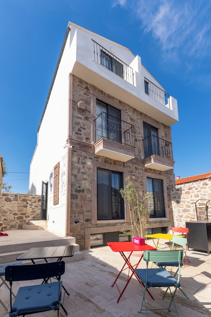 A two-story building with a stone facade, a balcony, and a patio area with outdoor furniture.
